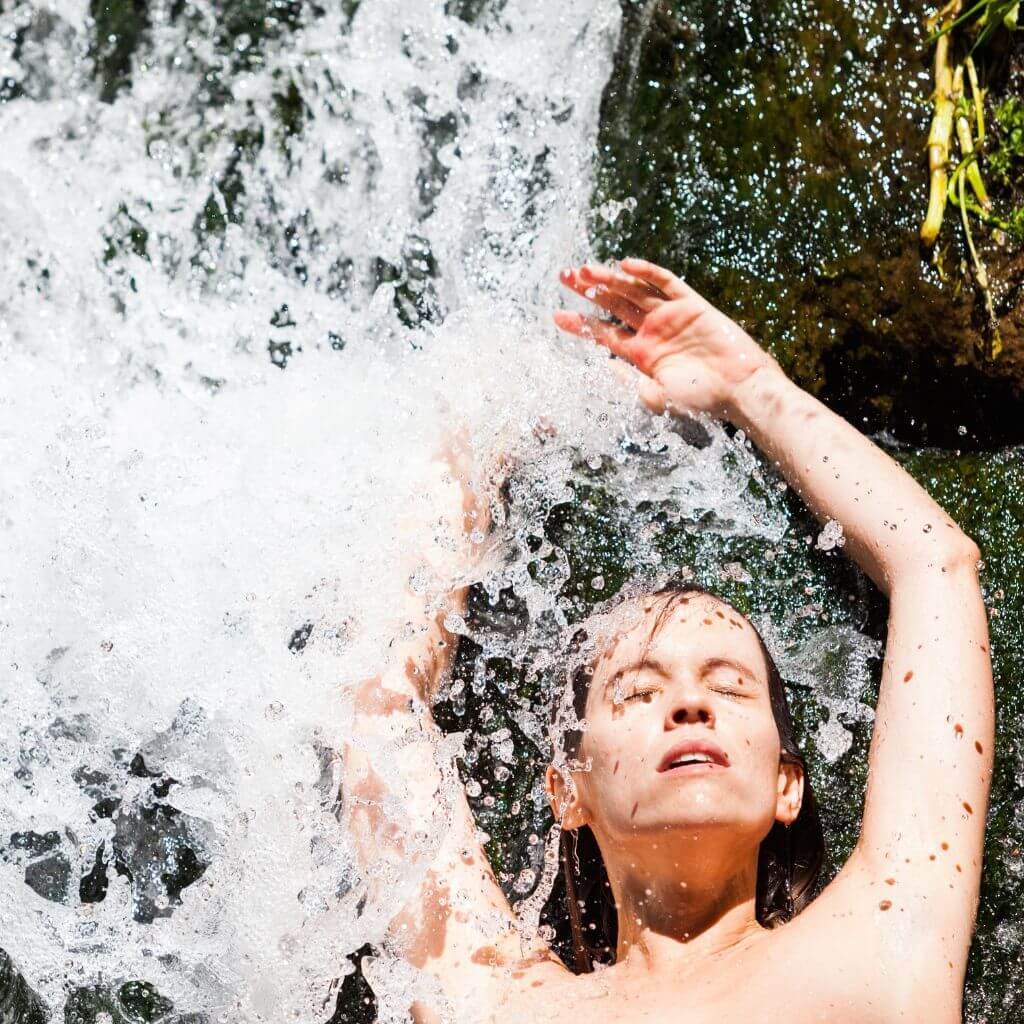 Myriam Peña bajo una cascada en plena activación corporal, introduciendo el módulo de Puntos Maestros de la Mujer en la Certificación en Sexualidad Femenina Taoísta – La Mujer Oceánica | Escuela de Mujeres