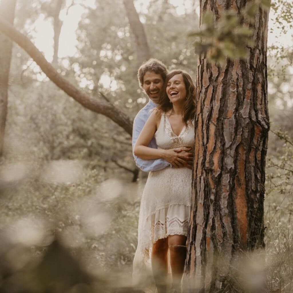 Myriam Peña y Agustín Reyes abrazados entre los árboles, mostrando complicidad y alegría, introduciendo el intensivo Sexualidad y Relaciones Conscientes – La Pareja Oceánica en la Certificación en Sexualidad Femenina Taoísta – La Mujer Oceánica | Escuela de Mujeres